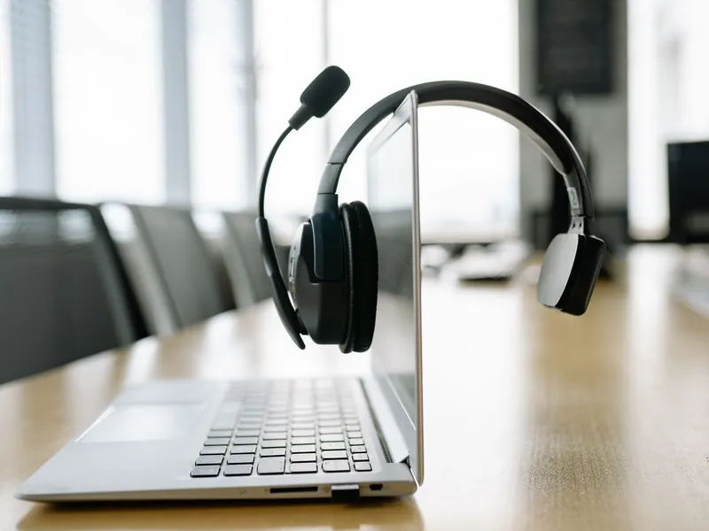 Laptop mit Headset auf einem hellen Büro-Tisch vor einer Fensterfront
